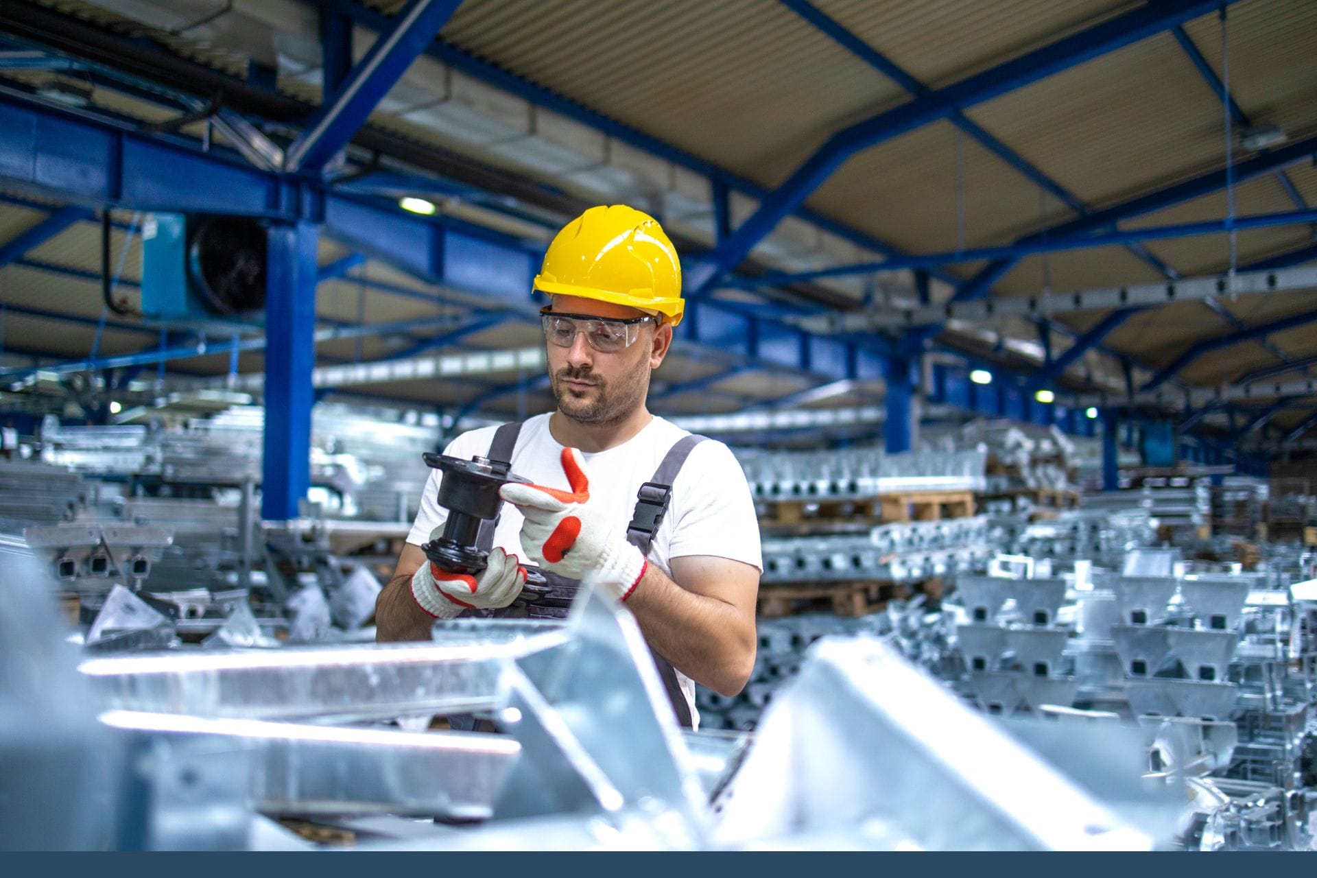 Man wearing a yellow hard hat and holding a tool in a warehouse environment.