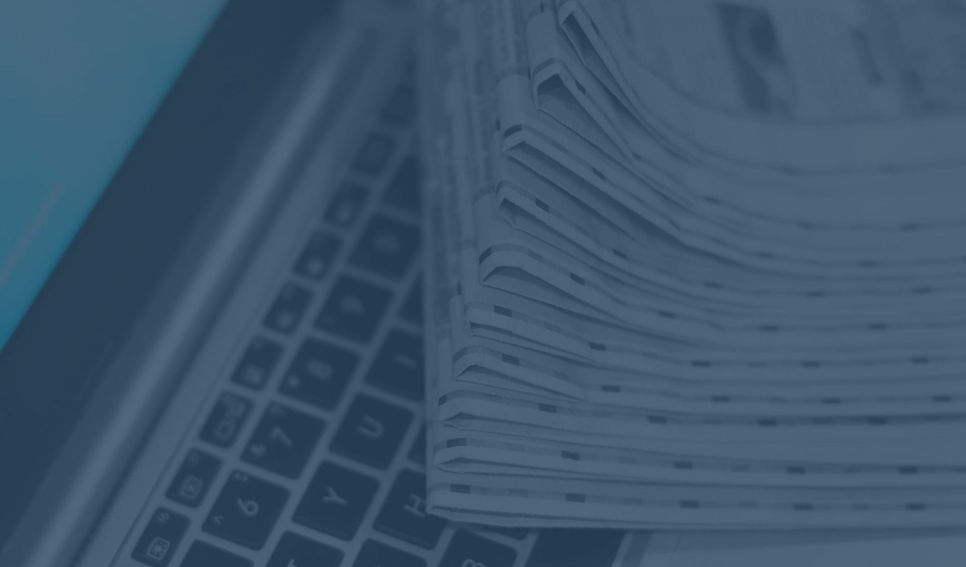 A pile of newspapers sits on top of a laptop keyboard